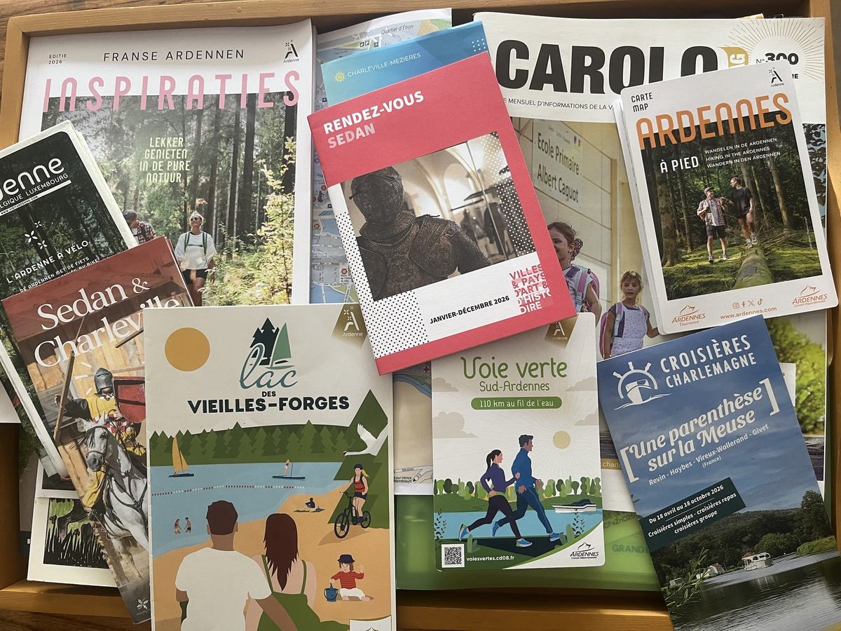 Des brochures touristiques des Ardennes sur un plateau en bois : Voie Verte, lac des Vieilles-Forges, Sedan et Charleville, croisières sur la Meuse.