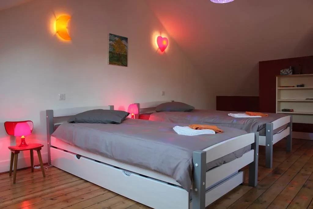 La chambre du second étage sous les combles : deux lits une personne, une applique en forme de lune, un cœur lumineux et une petite lampe rouge.