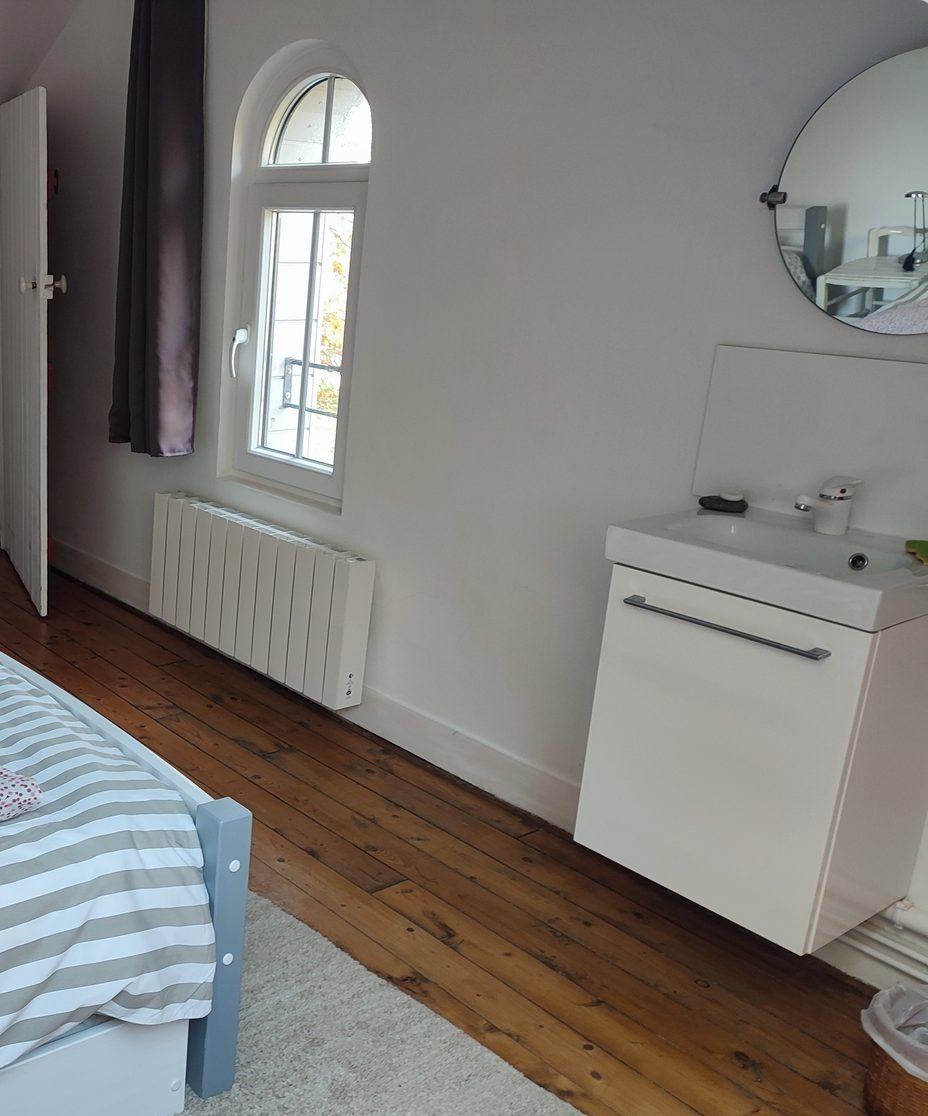 La chambre du second : le lavabo et son miroir rond près de la fenêtre cintrée, le lit et le parquet.