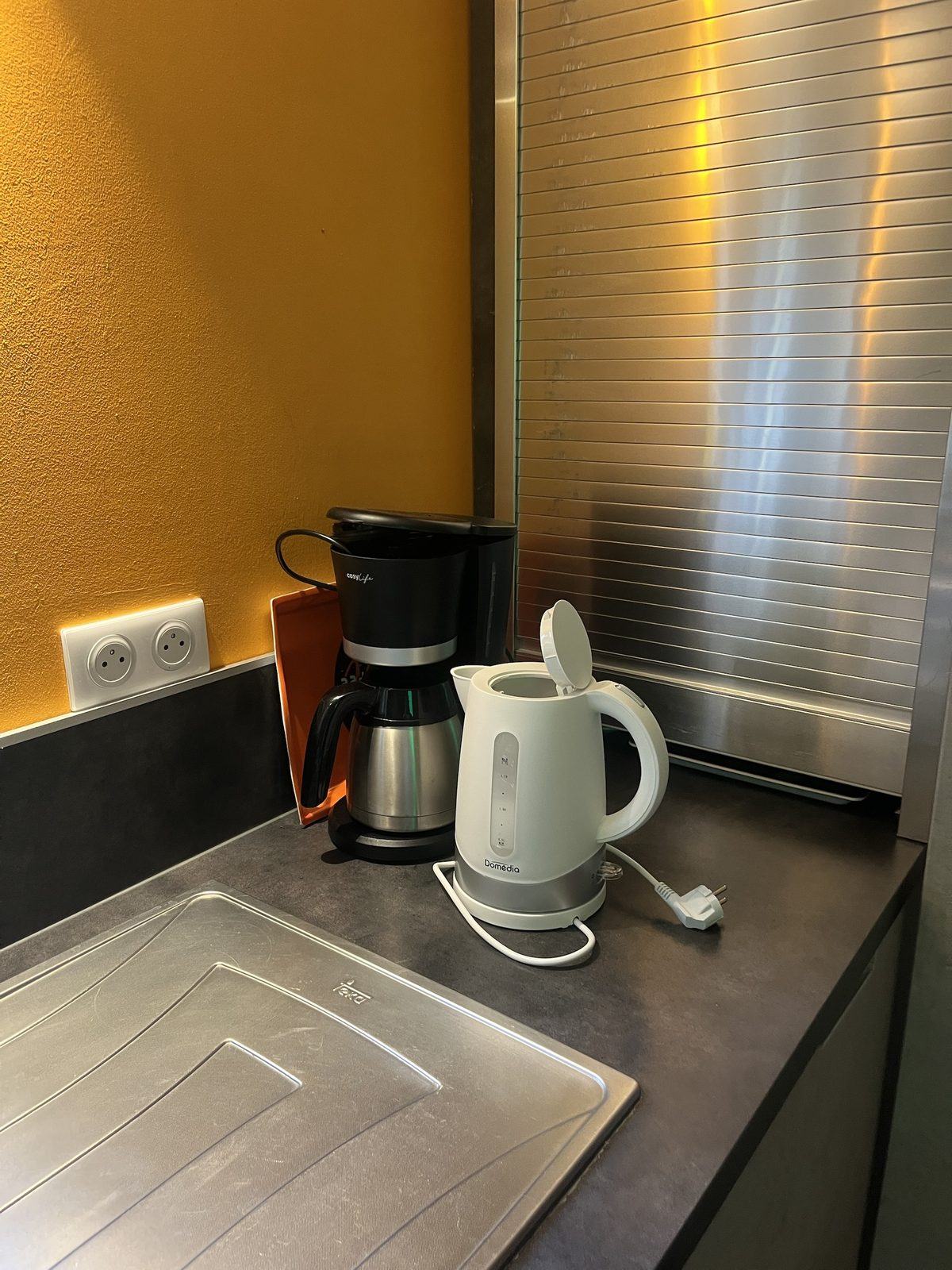Cafetière filtre isotherme et bouilloire électrique posées sur le plan de travail, devant le mur ocre.