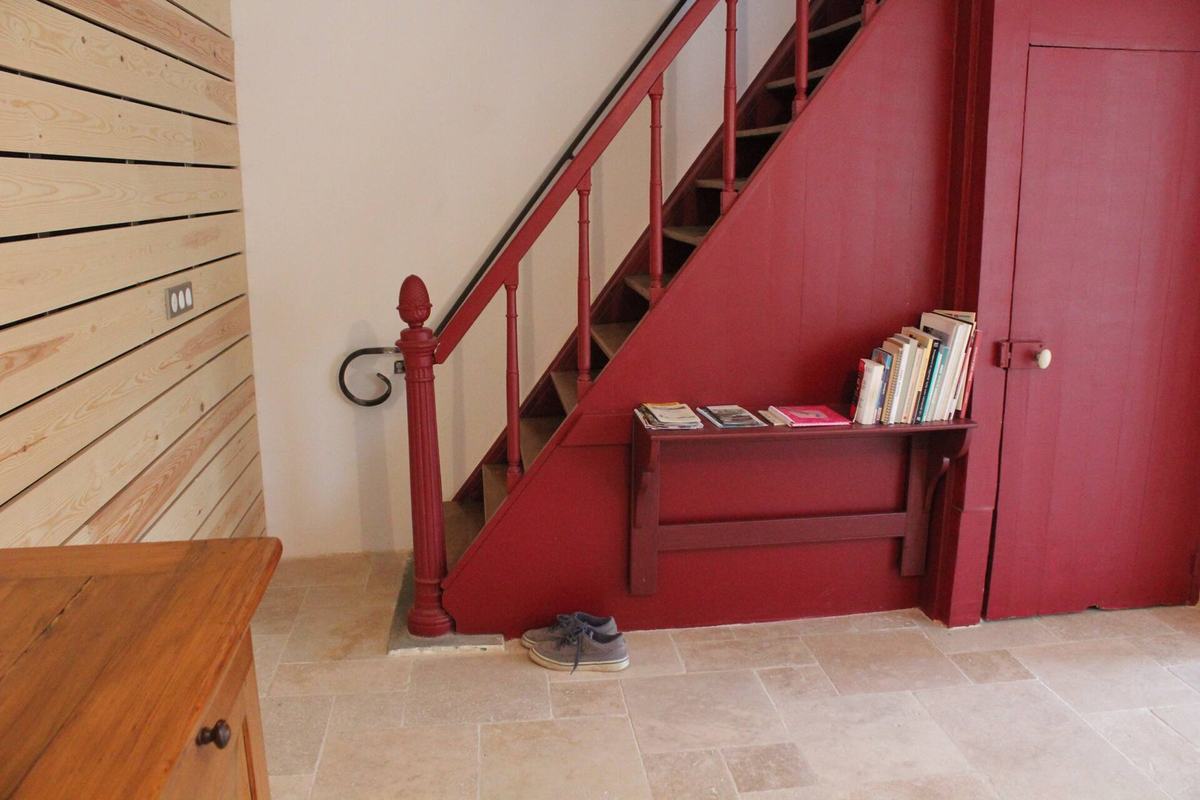 L’escalier de la maison, peint en rouge framboise, avec sa rampe en bois et une étagère à livres en dessous.