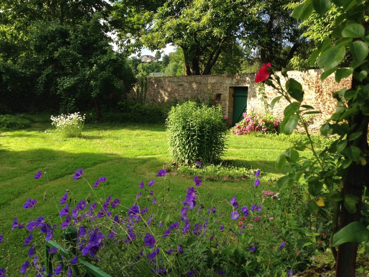 Le fond du jardin : pelouse, géraniums vivaces mauves, arbres et mur de pierre.