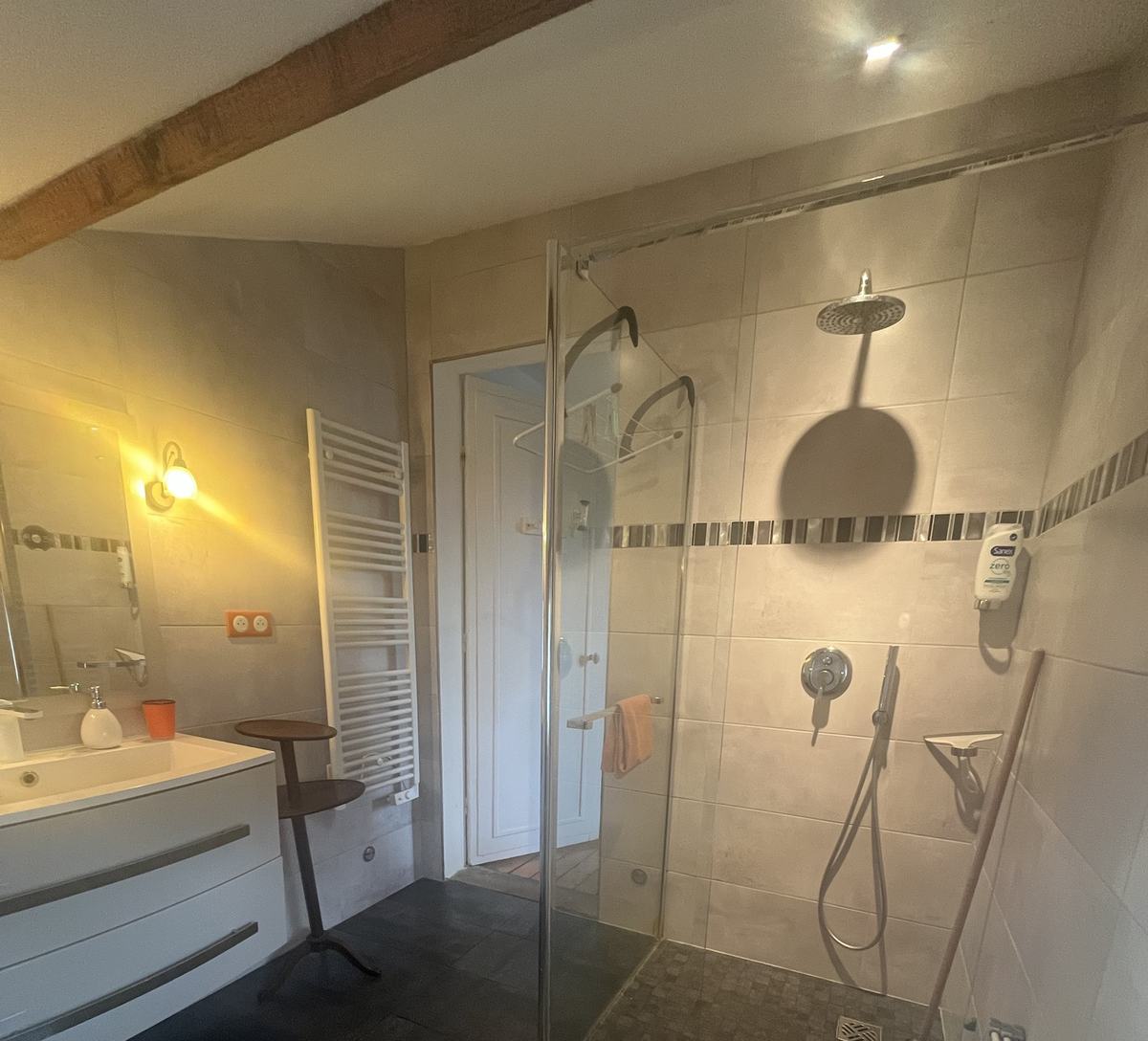 La salle de bain sous la poutre : douche à l’italienne, sèche-serviettes et meuble-vasque, sol en ardoise.