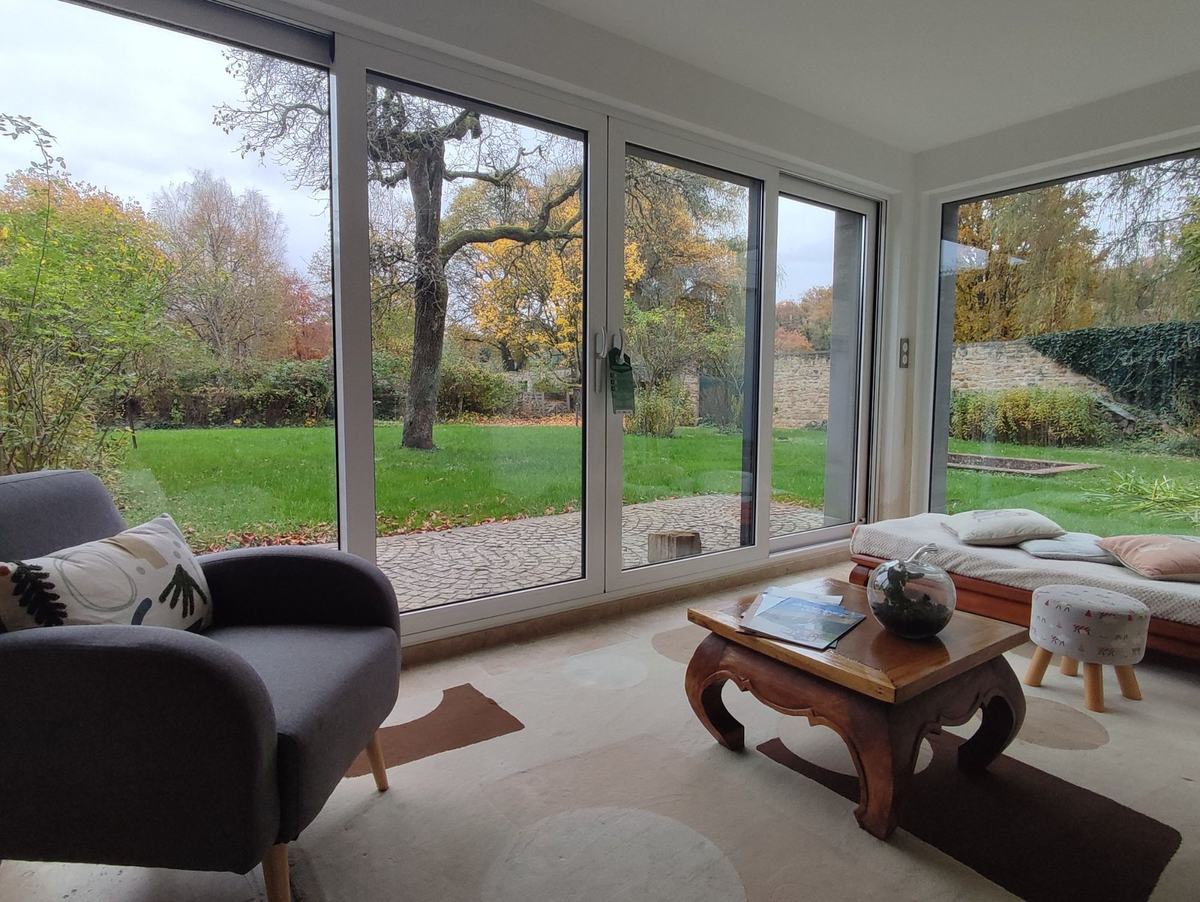 Le séjour en automne : les baies vitrées ouvertes sur le jardin aux feuillages jaunes, la table basse et la banquette.