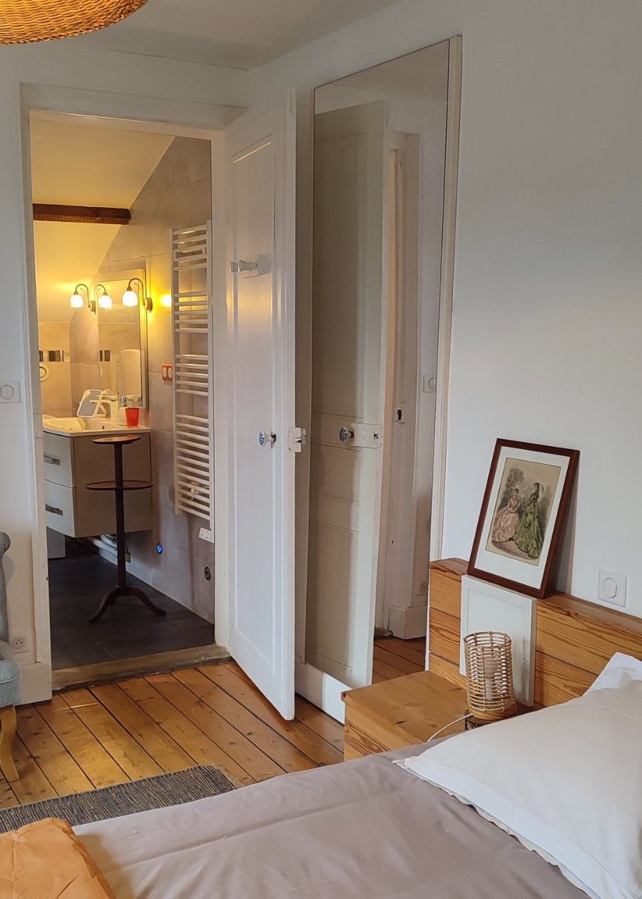 Depuis le lit de la chambre du premier, la porte ouverte sur la salle de bain : meuble-vasque, sèche-serviettes et appliques.