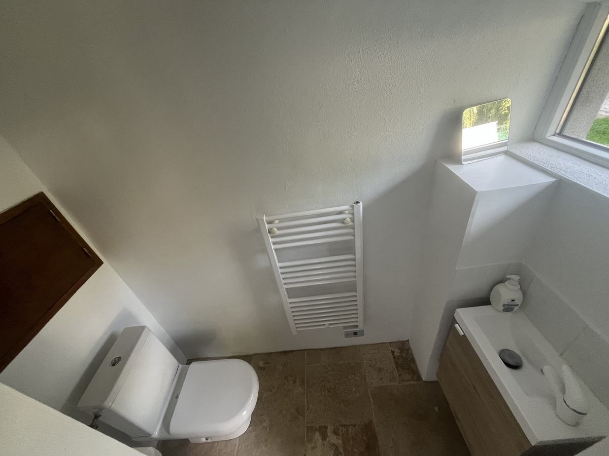 L’intérieur du second WC : cuvette, sèche-serviettes, lave-mains sur meuble en bois et petite fenêtre sur le jardin.